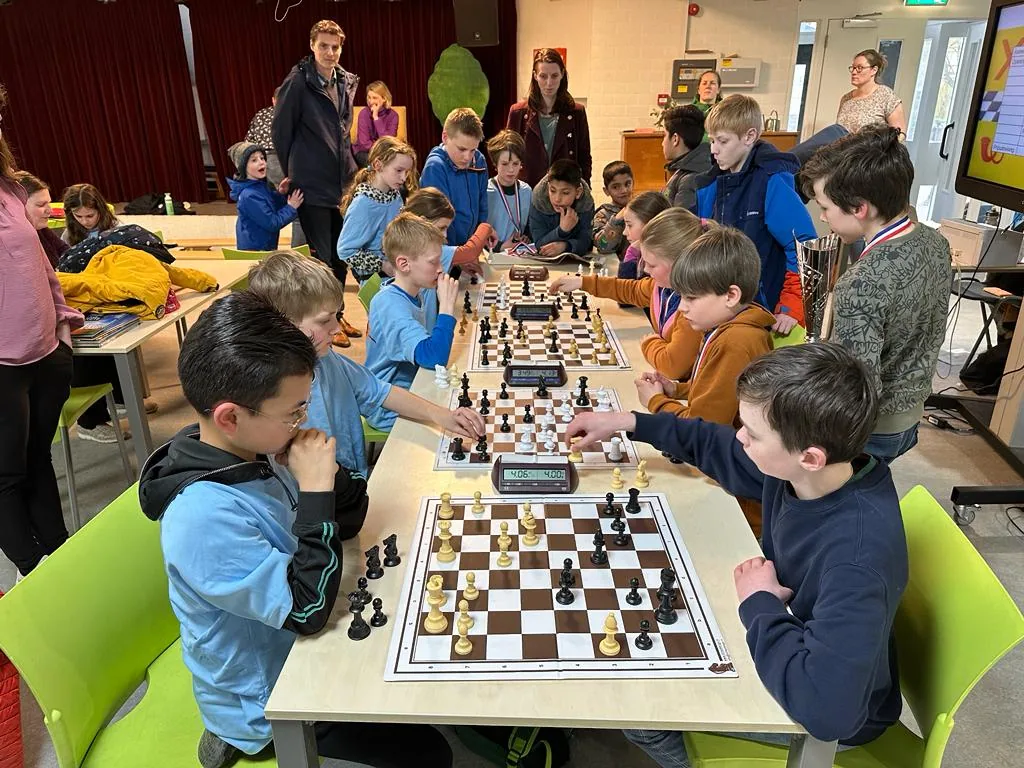 Een groep kinderen speelt schaakpartijen aan lange tafels