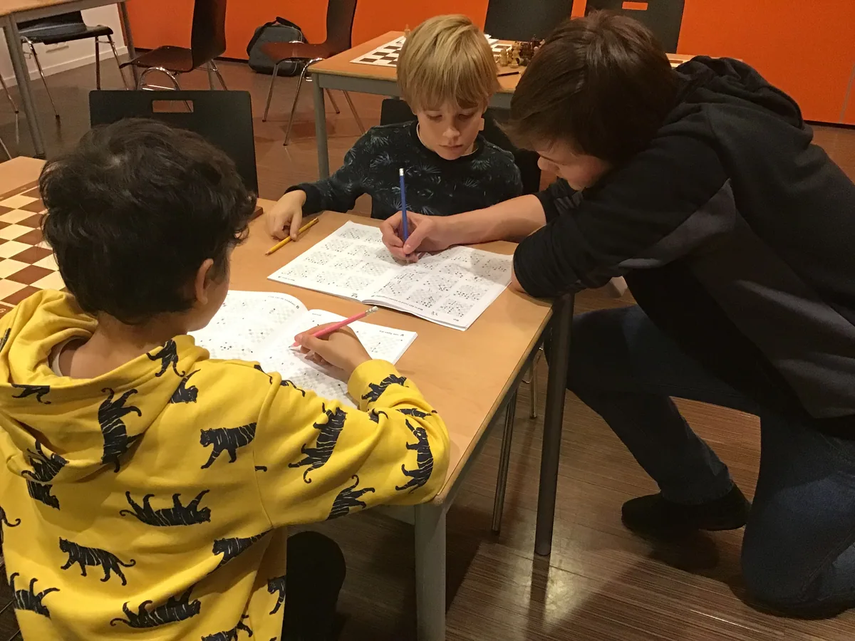Kinderen werken met een begeleider aan schaakoefeningen op papier